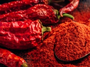 A close-up shot of a small composition of dried up chilli crops, placed alongside a wooden spoon filled with a red chilli powder, showcasing garden pest spicy trick