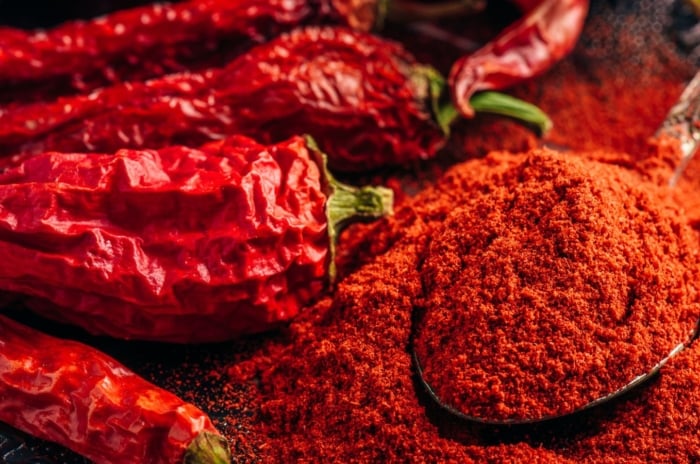 A close-up shot of a small composition of dried up chilli crops, placed alongside a wooden spoon filled with a red chilli powder, showcasing garden pest spicy trick