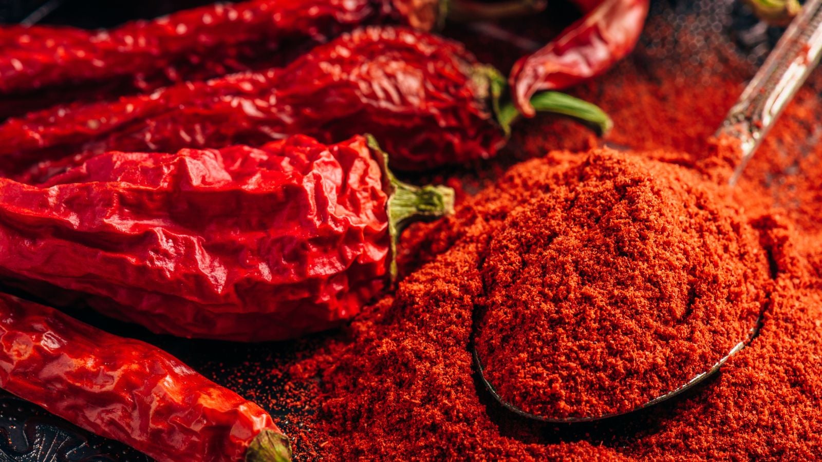 A close-up shot of a small composition of dried up chilli crops, placed alongside a wooden spoon filled with a red chilli powder, showcasing garden pest spicy trick