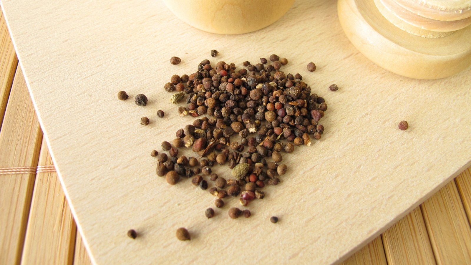 Small, rounded seeds in shades of brown are scattered across a textured wooden surface.
