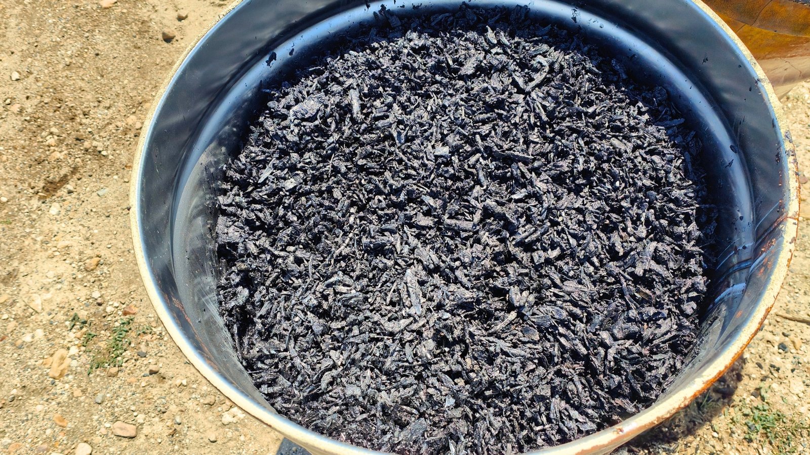 Close-up of chunky black biochar pieces inside a metal drum.