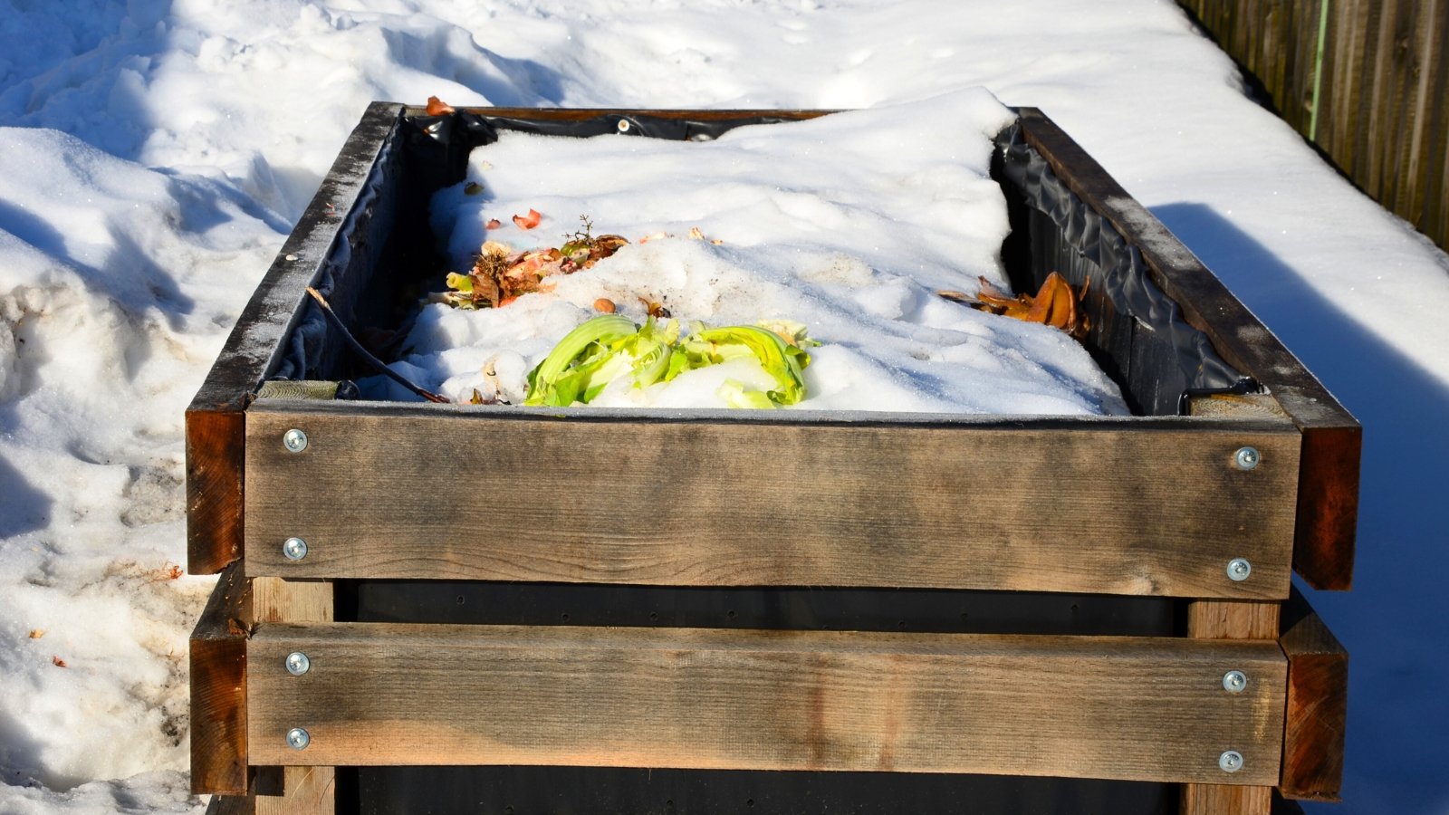 A wooden compost bin covered with a layer of white snow.