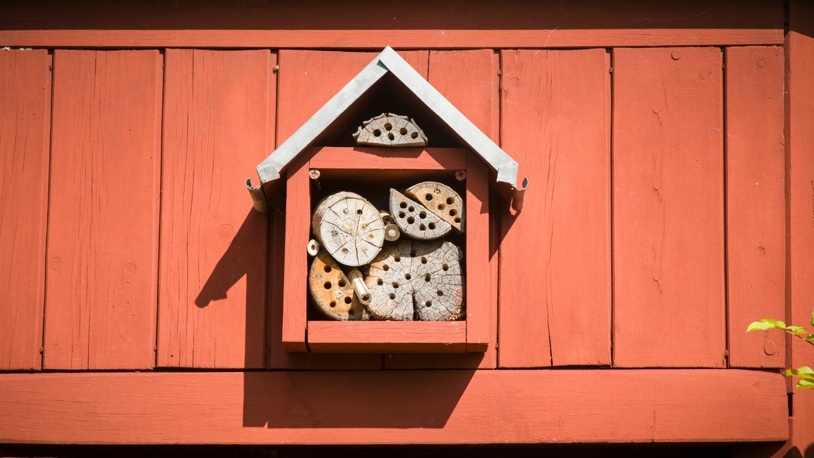 Wooden red insect house featuring stacked logs with drilled holes for nesting insects.