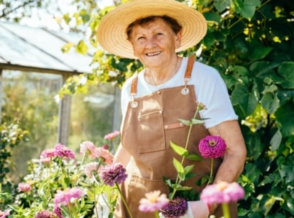 Italian nonna garden with the elder lady wearing a hat while holding plants with other greens in the background