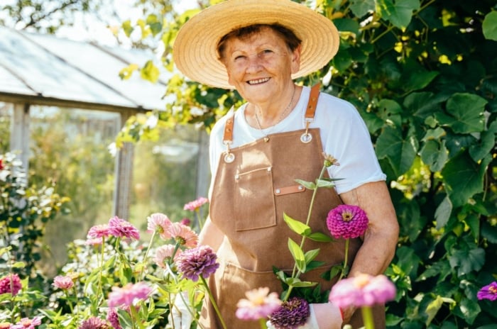 Italian nonna garden with the elder lady wearing a hat while holding plants with other greens in the background