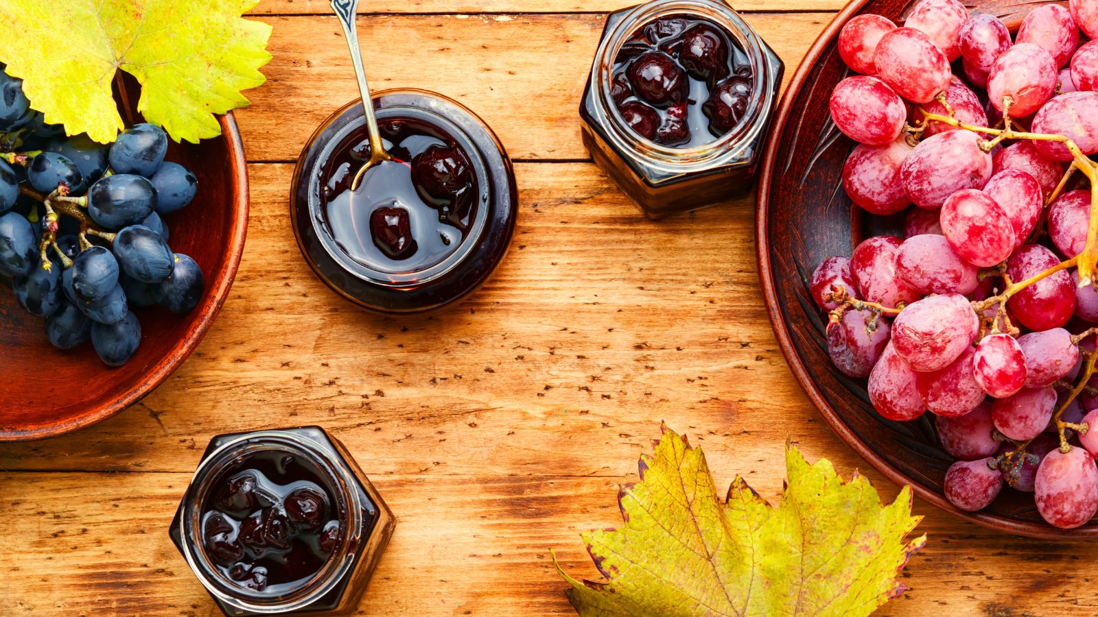 Multiple jars full of preserved Vitis vinifera, surrounded by plates with fresh purple berries on a wooden surface