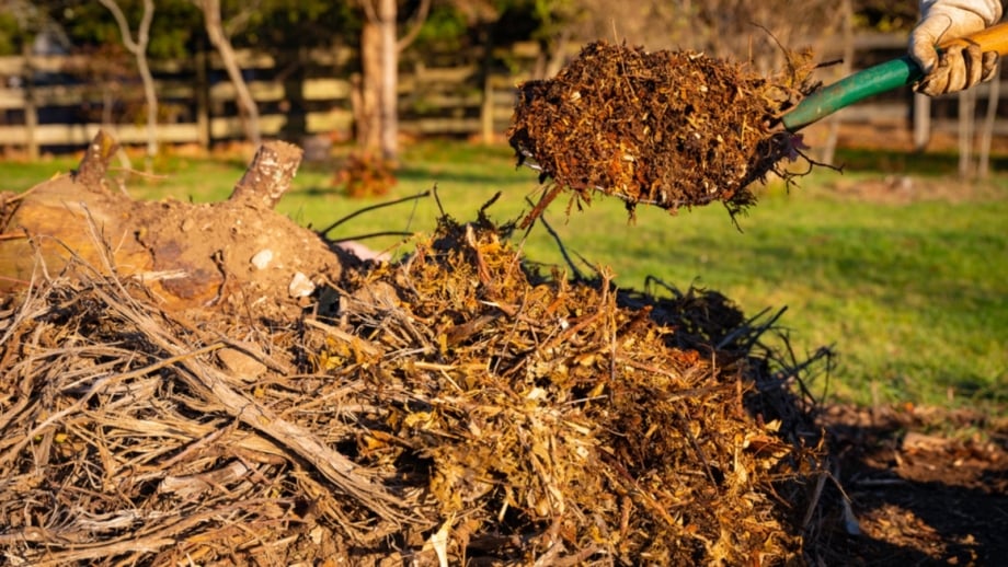 Gardener holding a spatula, building a raised Hugelkultur garden bed with layered soil and organic material.