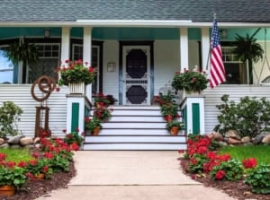 A fall porch with several pots of bright red mum alternatives with clustered petals and dark green leaves.