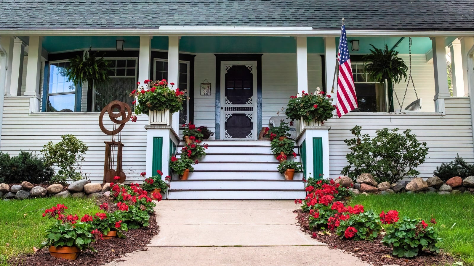 A fall porch with several pots of bright red mum alternatives with clustered petals and dark green leaves.