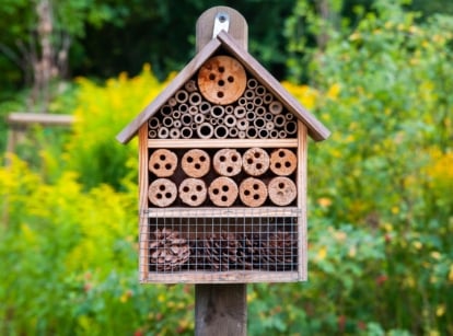Garden pollinator hotel with compartments filled with hollow stems, drilled wood, and natural materials for insects.
