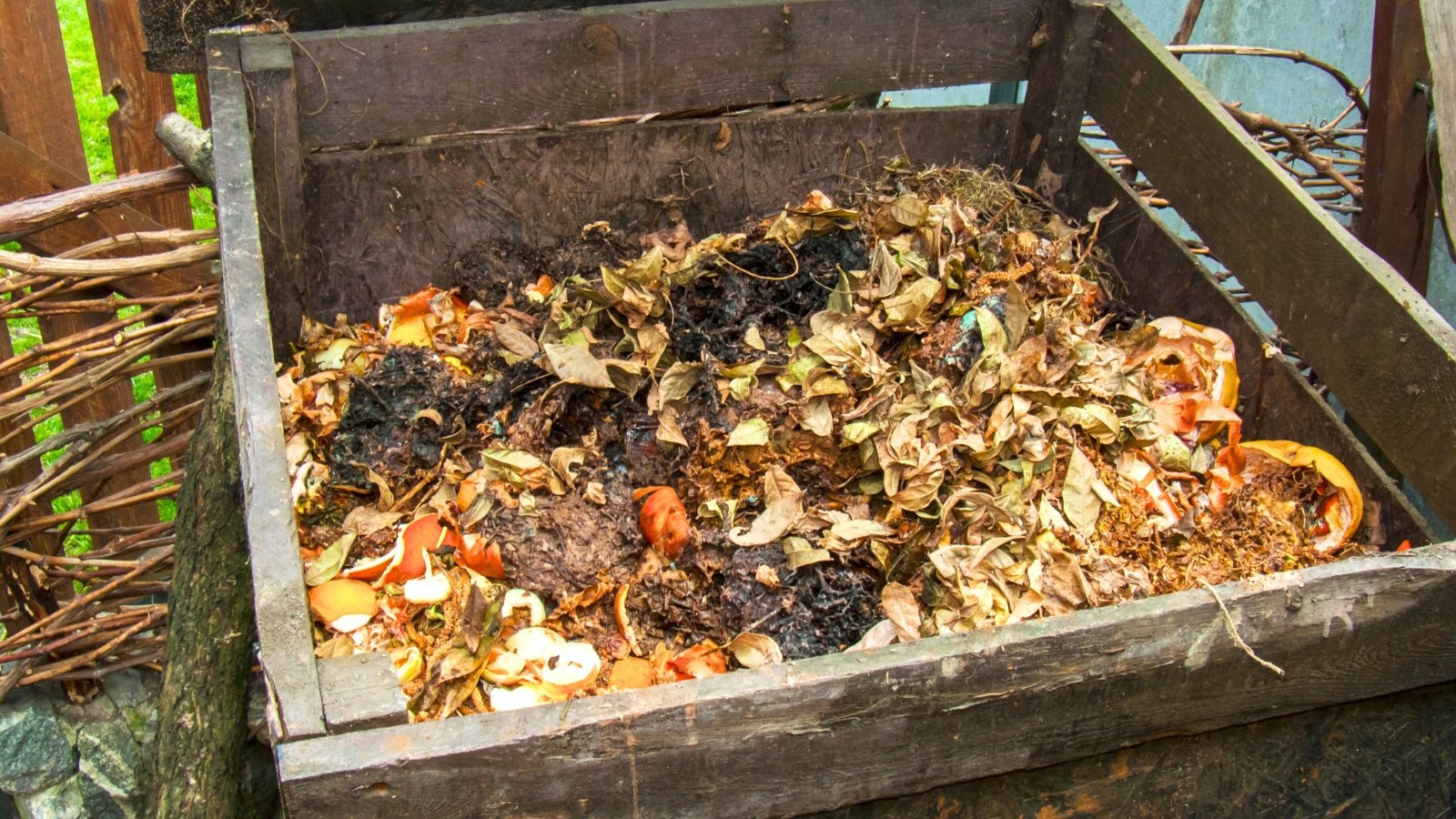 Wooden bin containing layers of kitchen scraps and dry leaves mixed with black charcoal pieces.