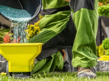 A man preparing to do fall lawn fertilizing, pouring the substance into a spreader to feed the lawn properly