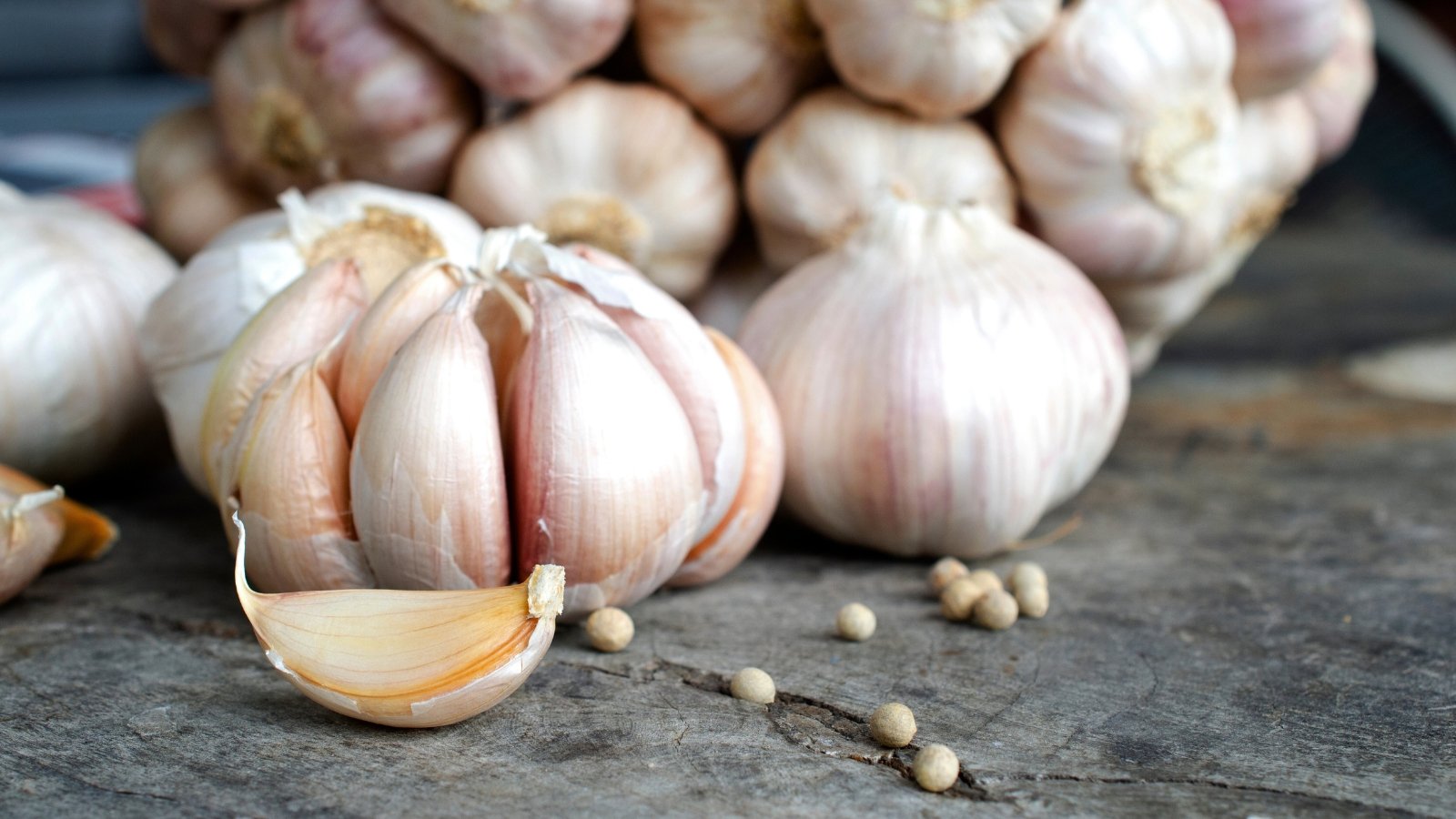 Garlic bulbs with multiple cloves rest on a wooden surface, their papery skins slightly peeling to reveal the pale flesh inside.