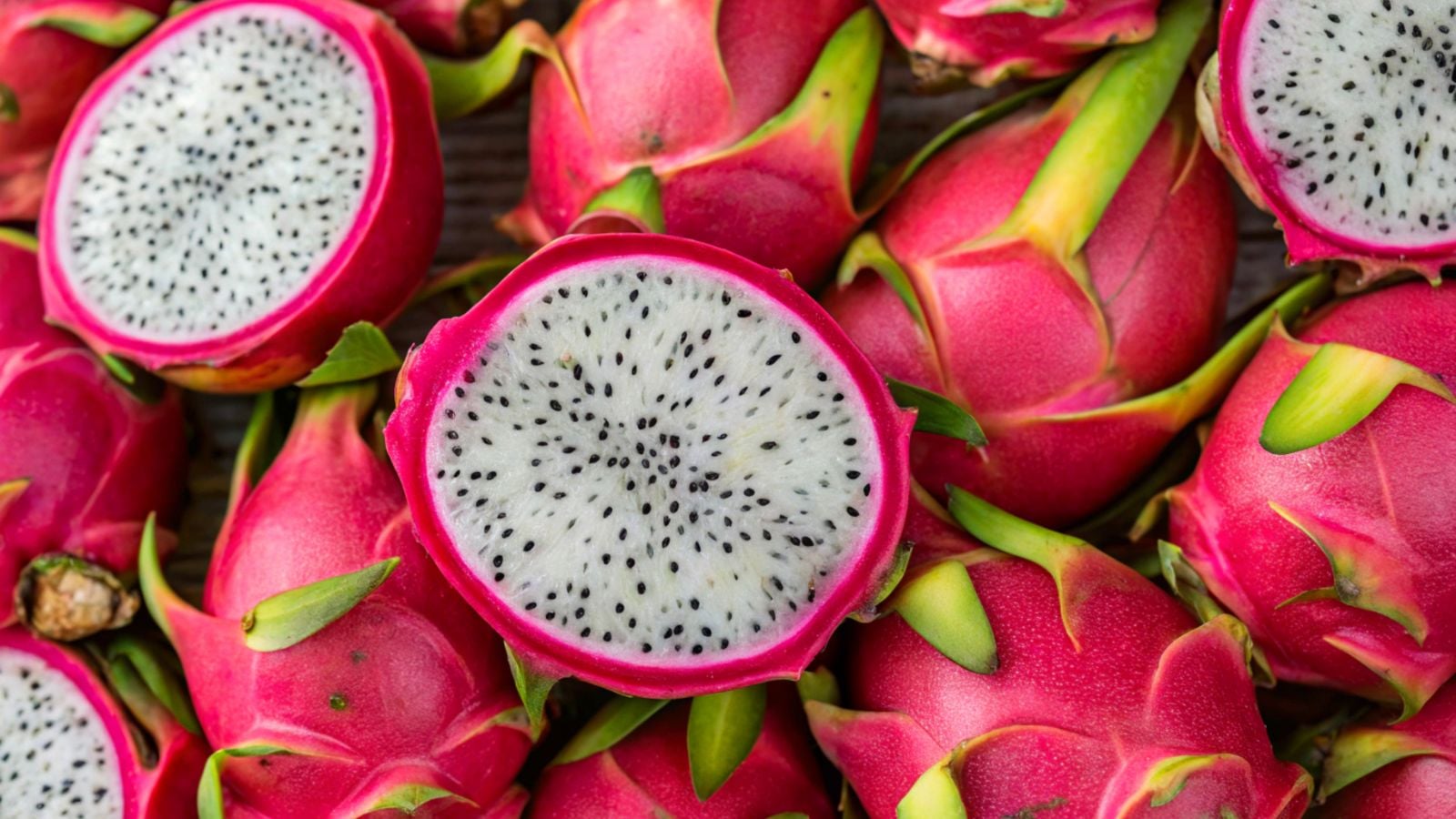 A pile of Hylocereus undatus ‘Vietnamese White’ fruits that appear pink with green scales, having pieces sliced open and placed on top of the pile