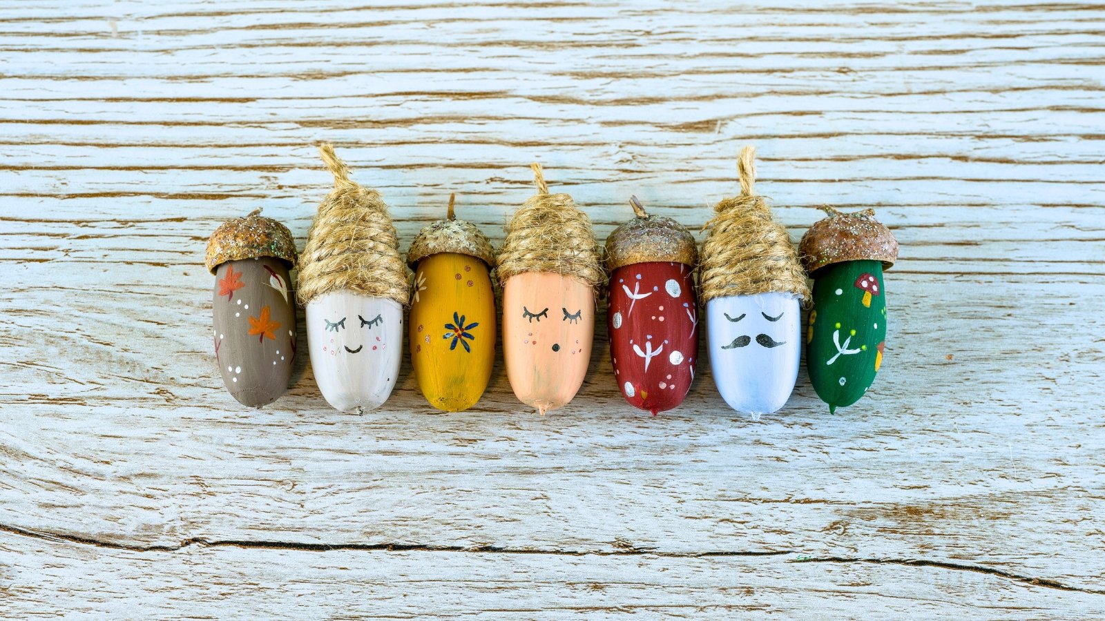 A row of painted acorns with their caps attached is arranged on a wooden surface, decorated with various patterns and faces.