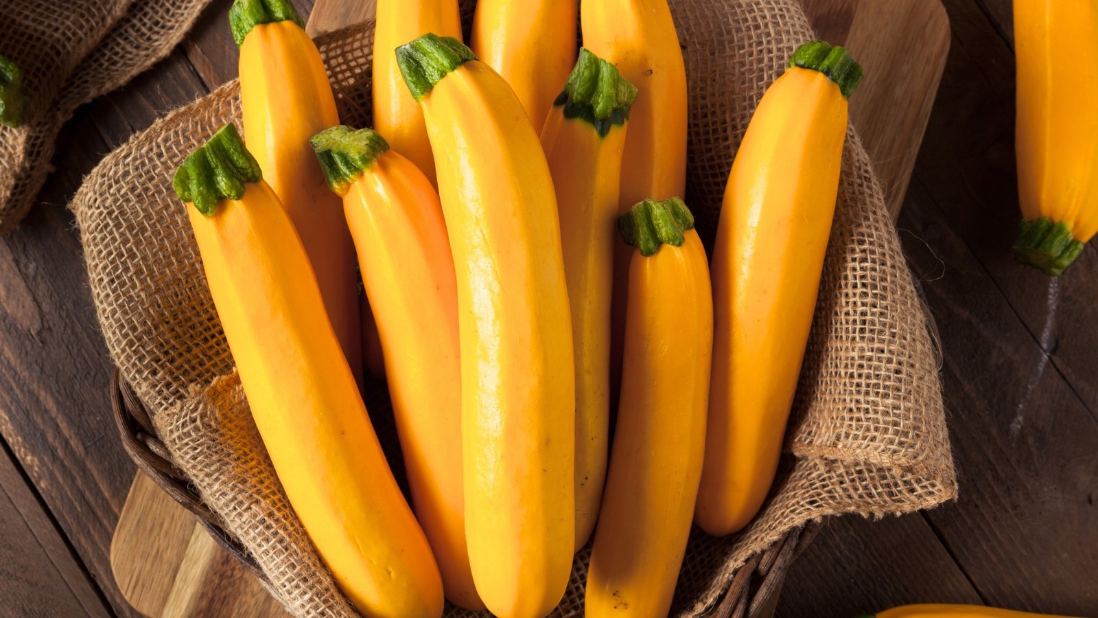 Oval-shaped, golden-yellow squash with smooth, slightly ribbed skin fill a rustic basket lined with burlap, resting on a wooden table.