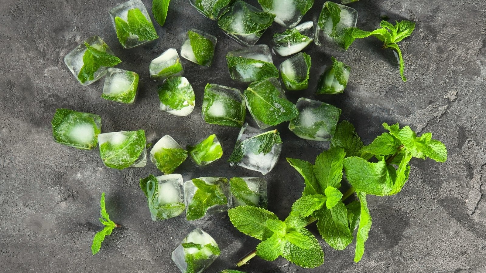 Fresh mint leaves are encased inside clear ice cubes on a wooden table, preserving their green color and texture.
