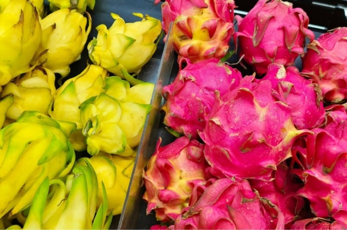 Showing dragon fruit varieties, with many fruits placed in piles and separated by color having one side with yellow fruits and the other with pink fruits