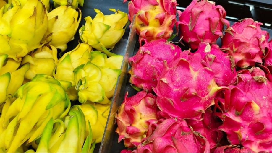 Showing dragon fruit varieties, with many fruits placed in piles and separated by color having one side with yellow fruits and the other with pink fruits