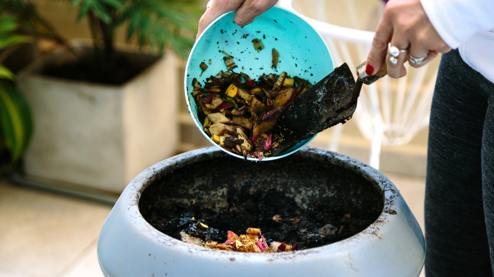 A woman on a balcony empties kitchen scraps from a bowl into a compost bin, starting the process of composting in a small urban space.