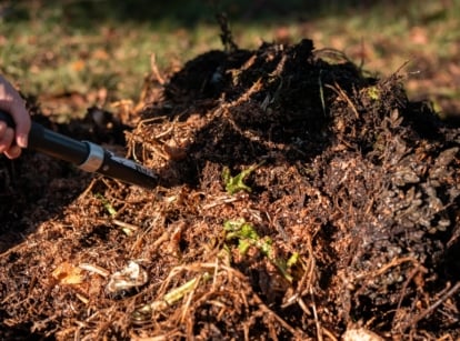 A gardener uses a garden pitchfork to turn a steaming heap of organic matter in an autumn setting, illustrating october composting in progress.