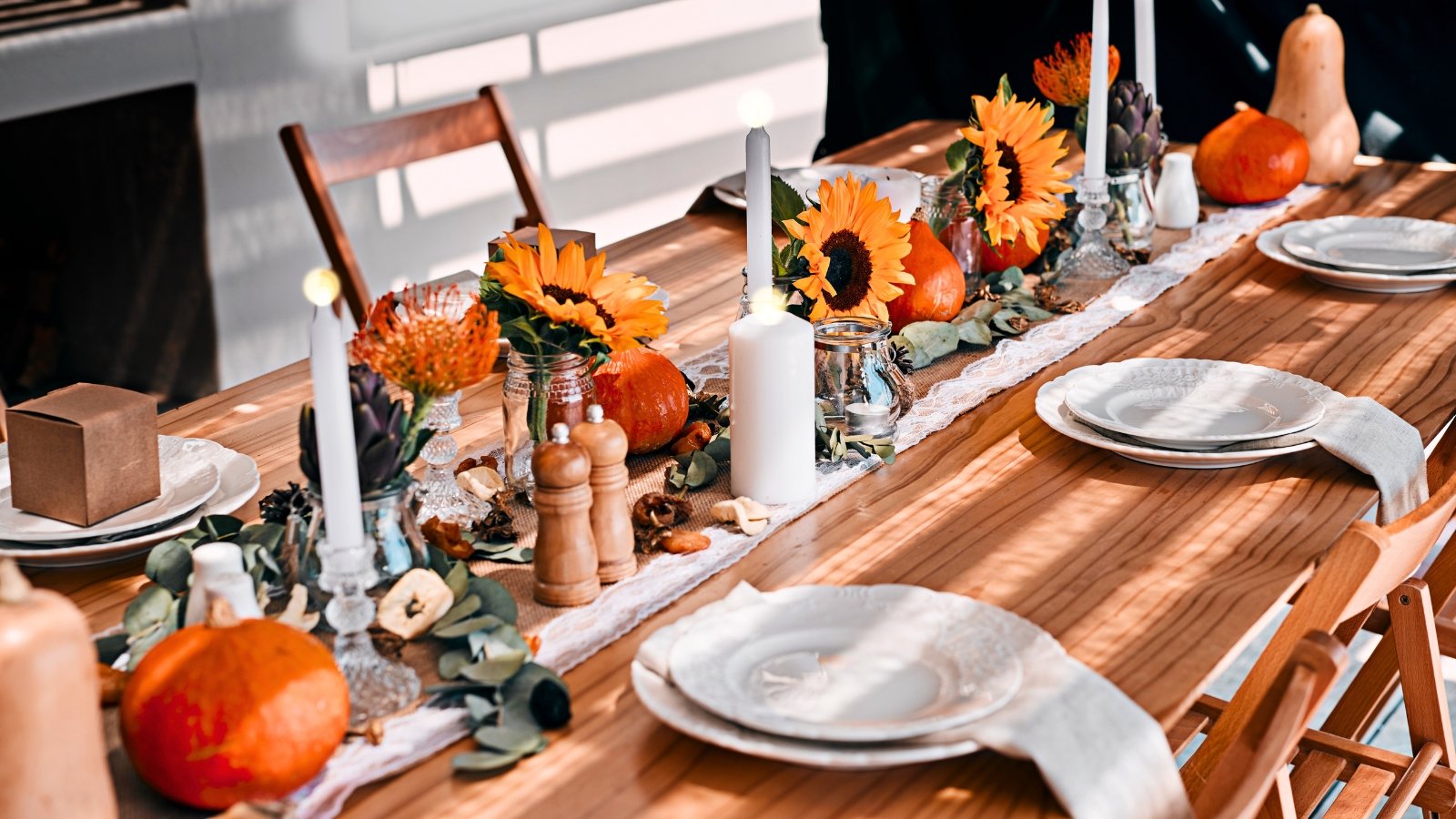 A festive table runner holds a centerpiece featuring miniature pumpkins, sunflowers, and small bunches of leucospermum (pincushion flowers).