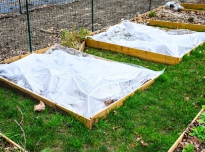 The winterized garden shows rows of wooden raised beds, some covered with white row covers and others layered with leaf mulch.