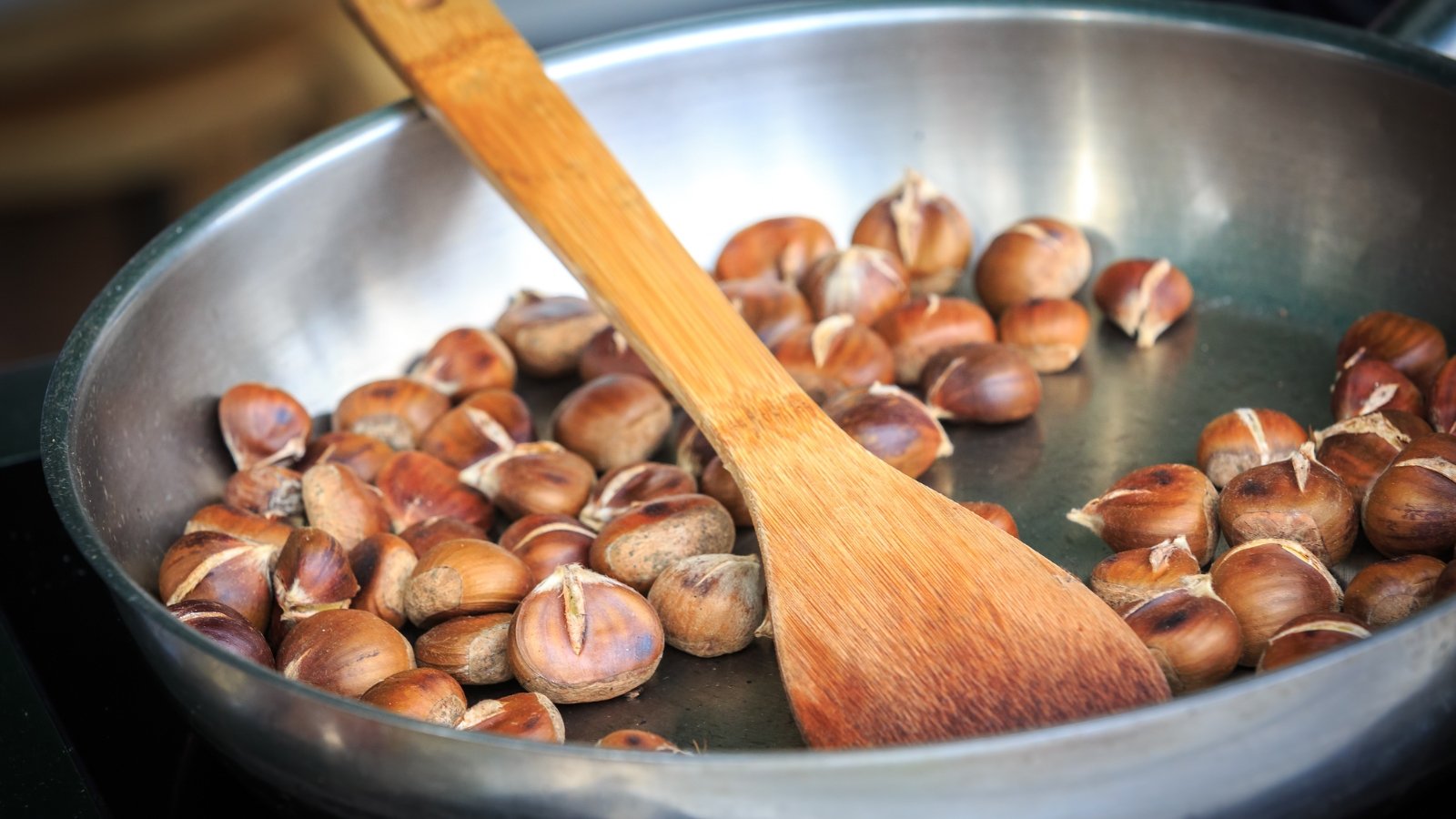 Pan is filled with golden-brown fried chestnuts, with a wooden spatula.
