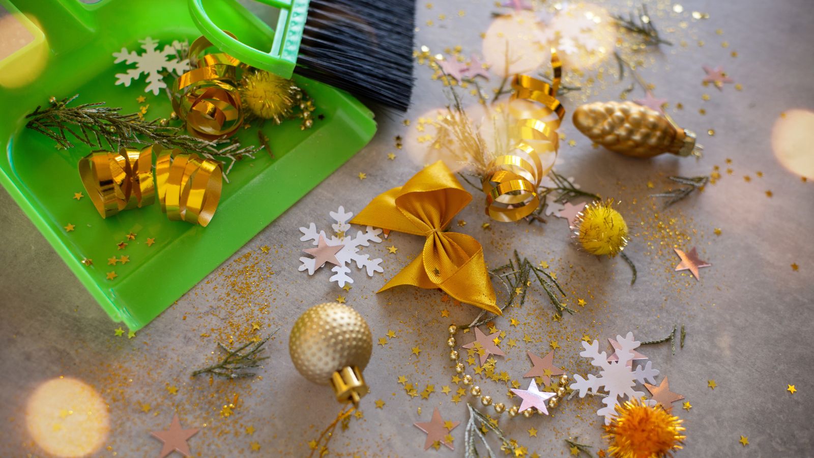 An overhead shot of several ornaments and debris, all placed on the floor and being swept, using small green dustpan and broom, all situated in a well lit area