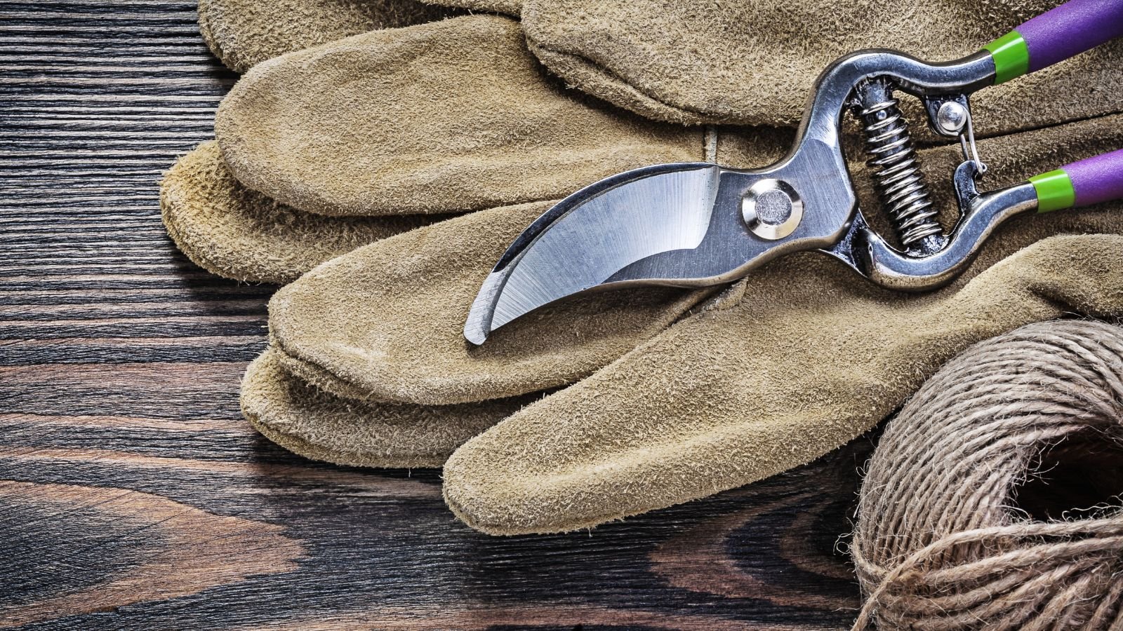 A shot of gloves and pruners placed on a wooden table appearing to be made of wood with a ball of string lay beside them