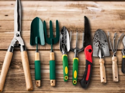 A close-up and overhead shot of a composition of gardening tools, placed on a wooden surface, showcasing garden tools before using