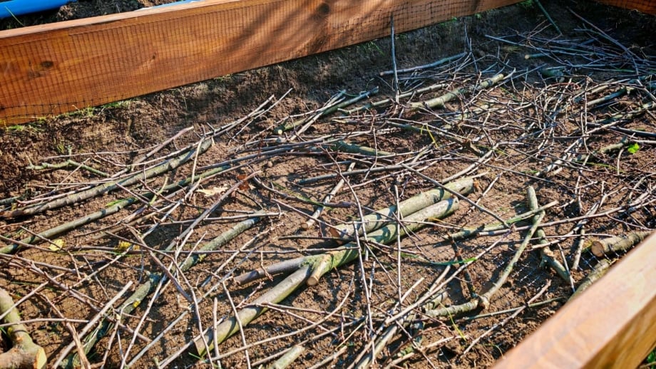 A close-up and overhead shot of a small composition of wood, placed on top of rich soil on a large planter, showcasing winter branches raised beds