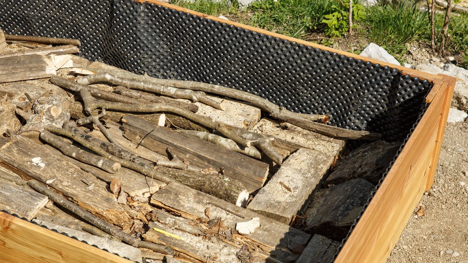 A close-up and overhead shot of several large and small wooden limbs, piled on top of each other, all placed on a large planter
