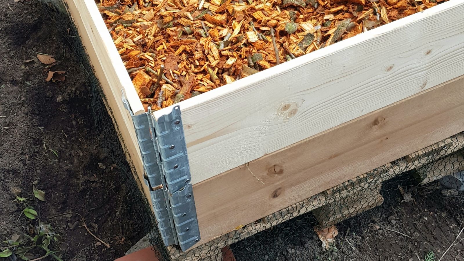 A close-up shot of a corner end of a large wooden planter placed on a rich dark soil in a garden area