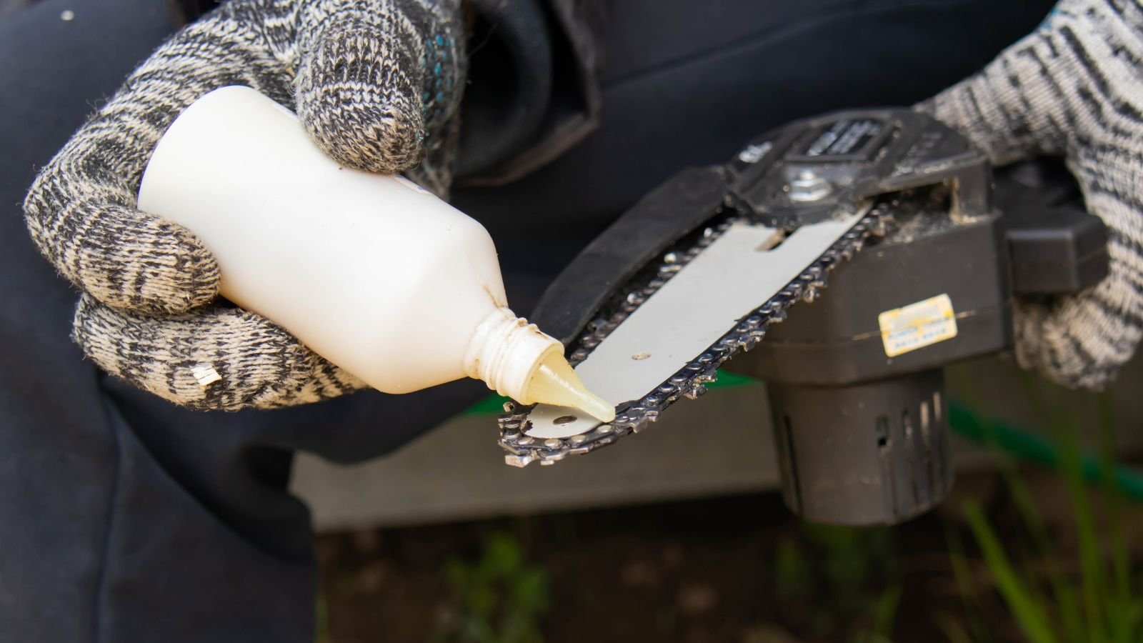 A close-up shot of a person in the process of oiling and lubricating a small electric saw, all situated in a well lit area outdoors