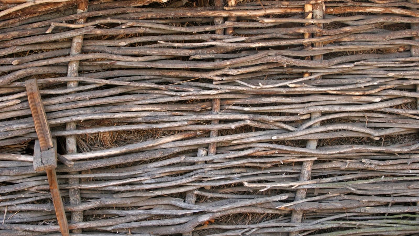 A close-up shot of a woven, wooden, DIY planter, all situated in a well lit garden area outdoors