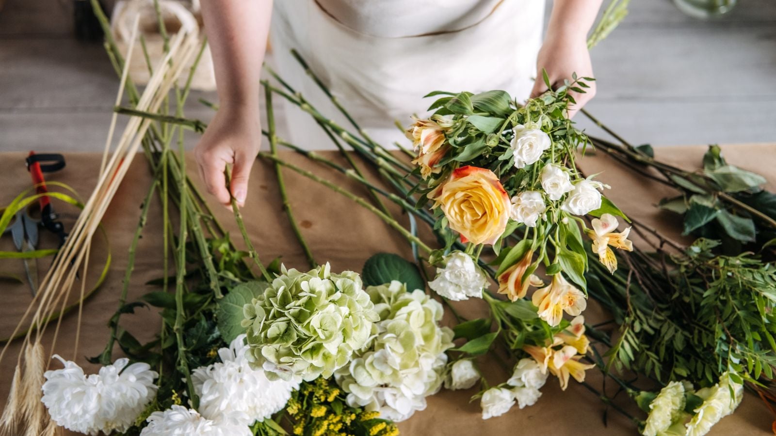 A close-up and overhead shot of a person in the process of arranging cuttings of blossoms, all situated in a well lit area indoors