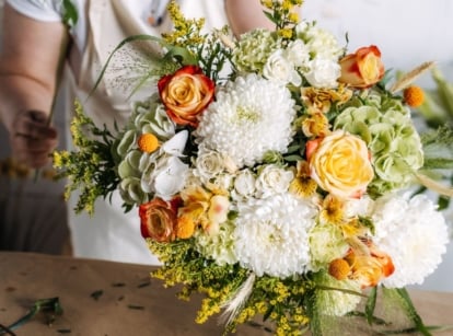 A close-up shot of a florist in the process of arranging blooms, all placed on a wooden surface, showcasing how to grow wedding flowers