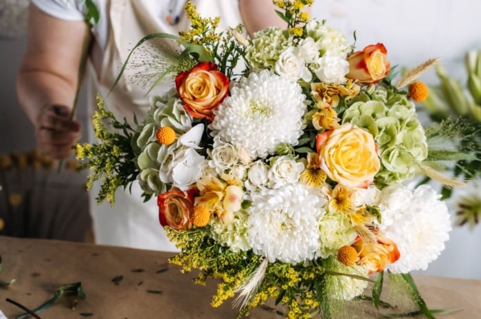 A close-up shot of a florist in the process of arranging blooms, all placed on a wooden surface, showcasing how to grow wedding flowers