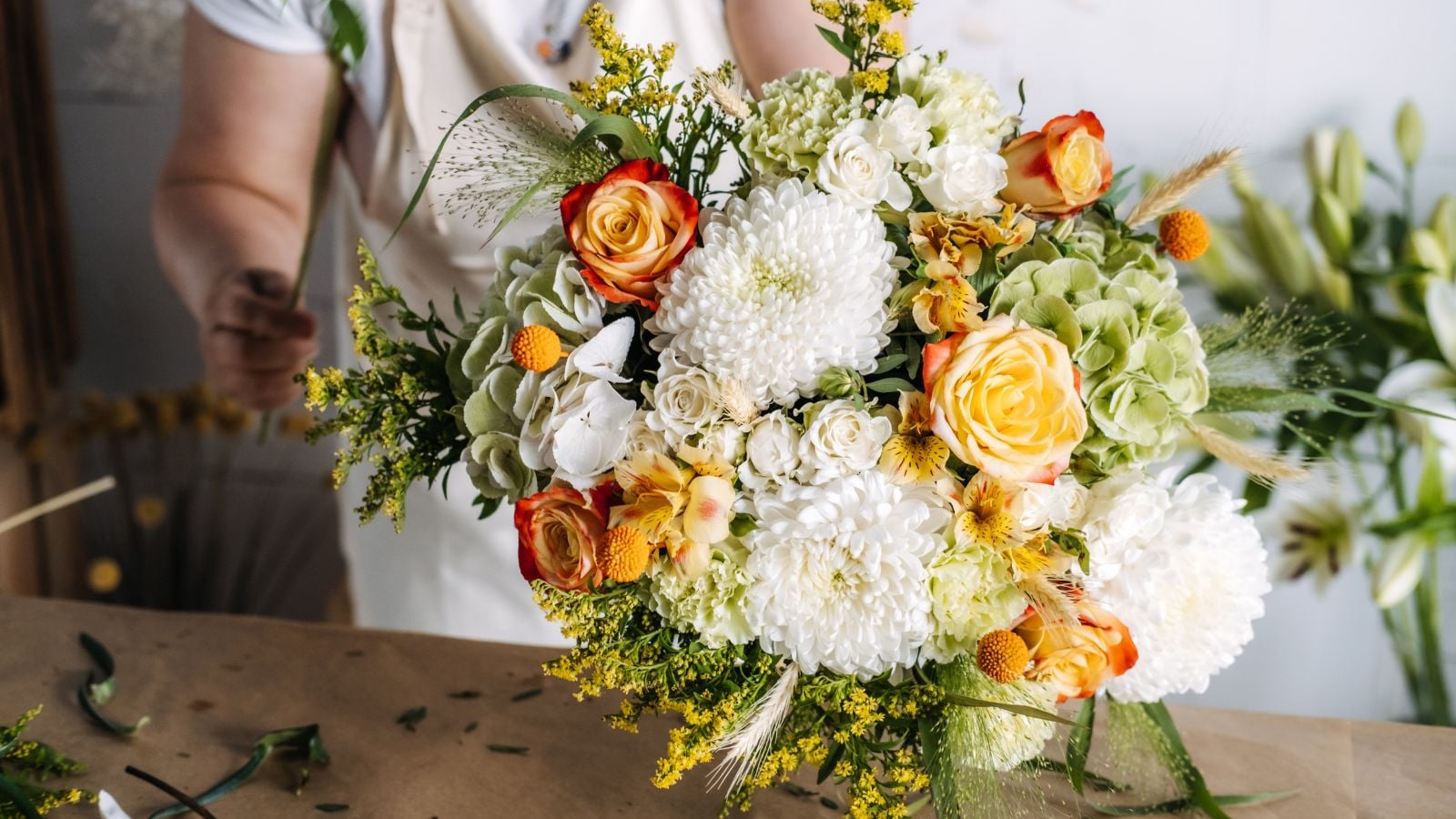 A close-up shot of a florist in the process of arranging blooms, all placed on a wooden surface, showcasing how to grow wedding flowers
