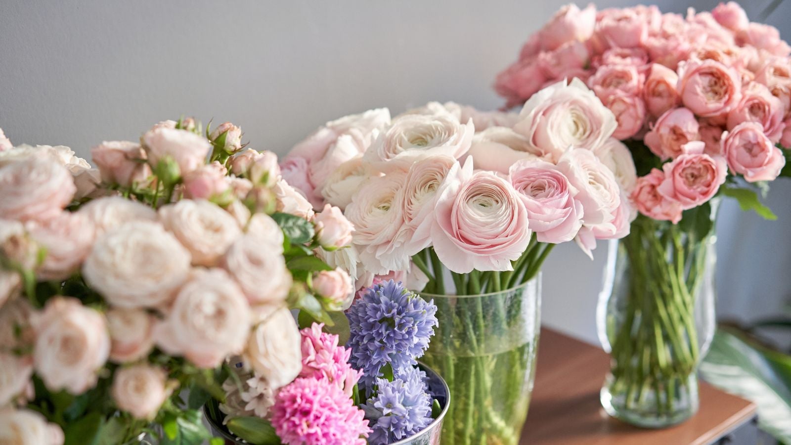 A close-up shot of several cuttings of peony and zinnia blooms placed on large jars filled with water, all situated in a well lit area indoors