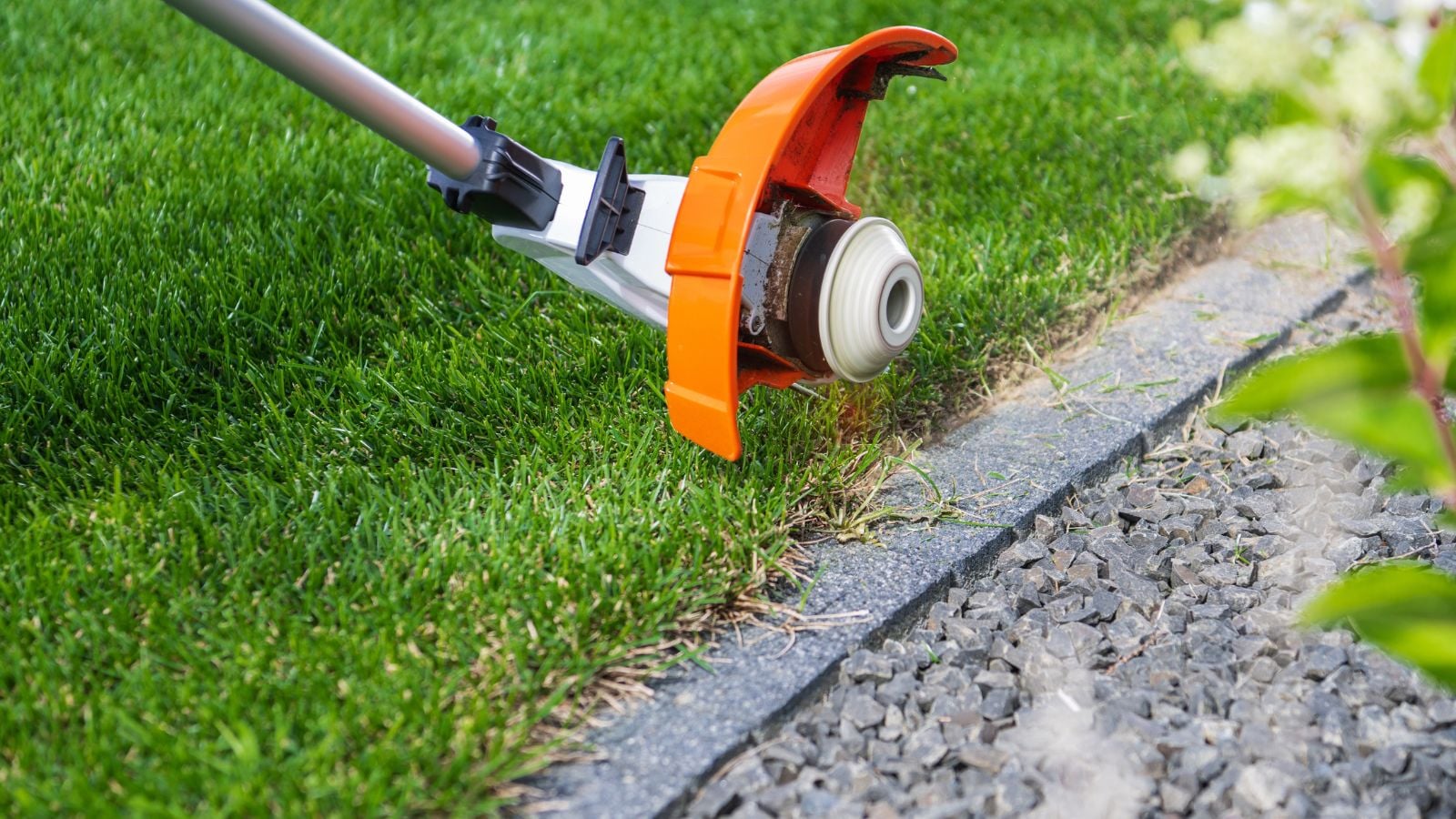 A close-up shot of an electric weed whacker being used to clean and trim borders of a turf alongside a stone walkway outdoors 
