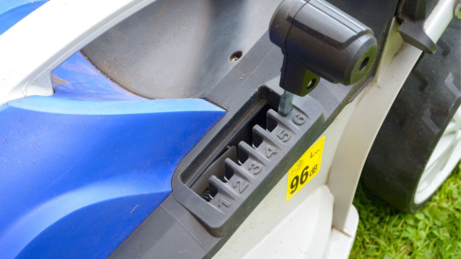 A close-up and overhead shot of lever of a blue colored mower to adjust height, all placed in a well lit area outdoors