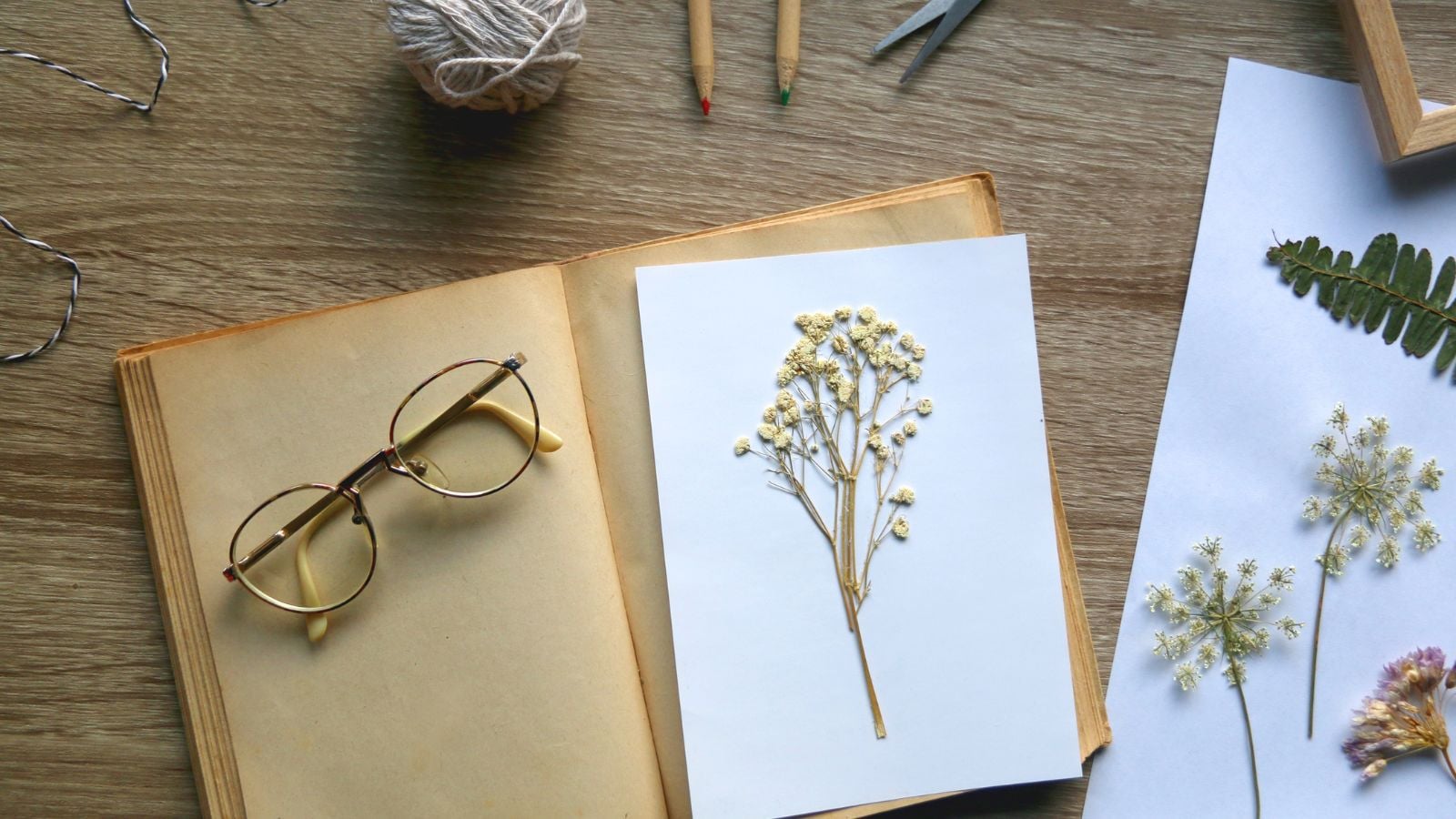A close-up and overhead shot of DIY Pressed Flower Cards placed beside several tools and a notebook in a well lit area indoors
