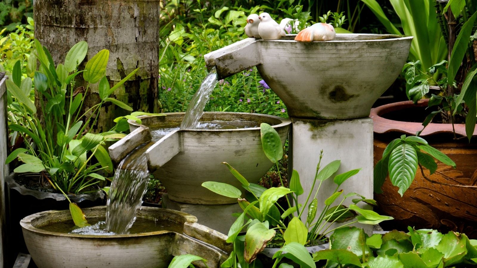 A close-up shot of a simple stone decorative water feature, placed alongside potted plants in a well lit area outdoors